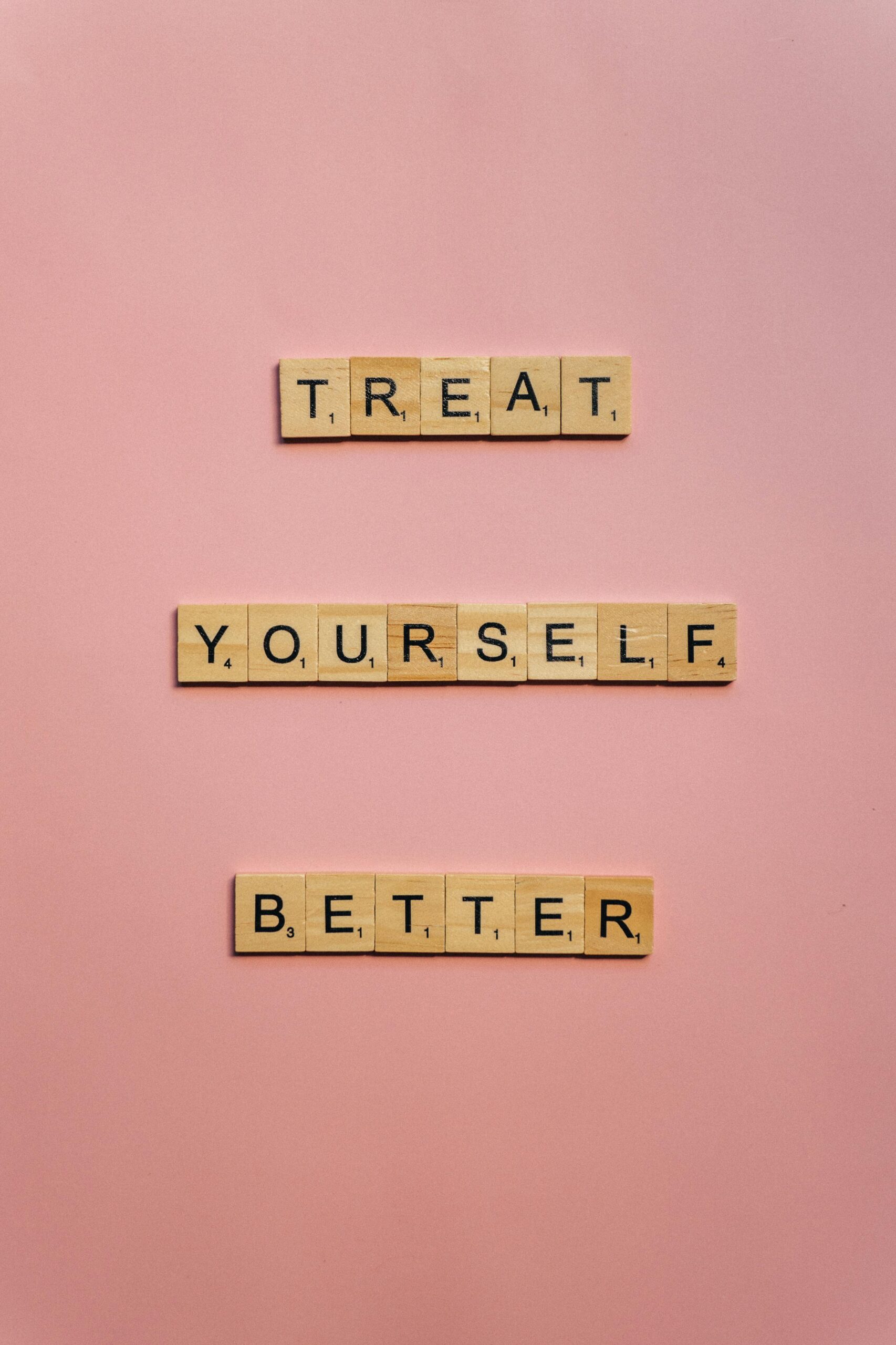 Scrabble tiles spelling 'Treat Yourself Better' on a pink background.
