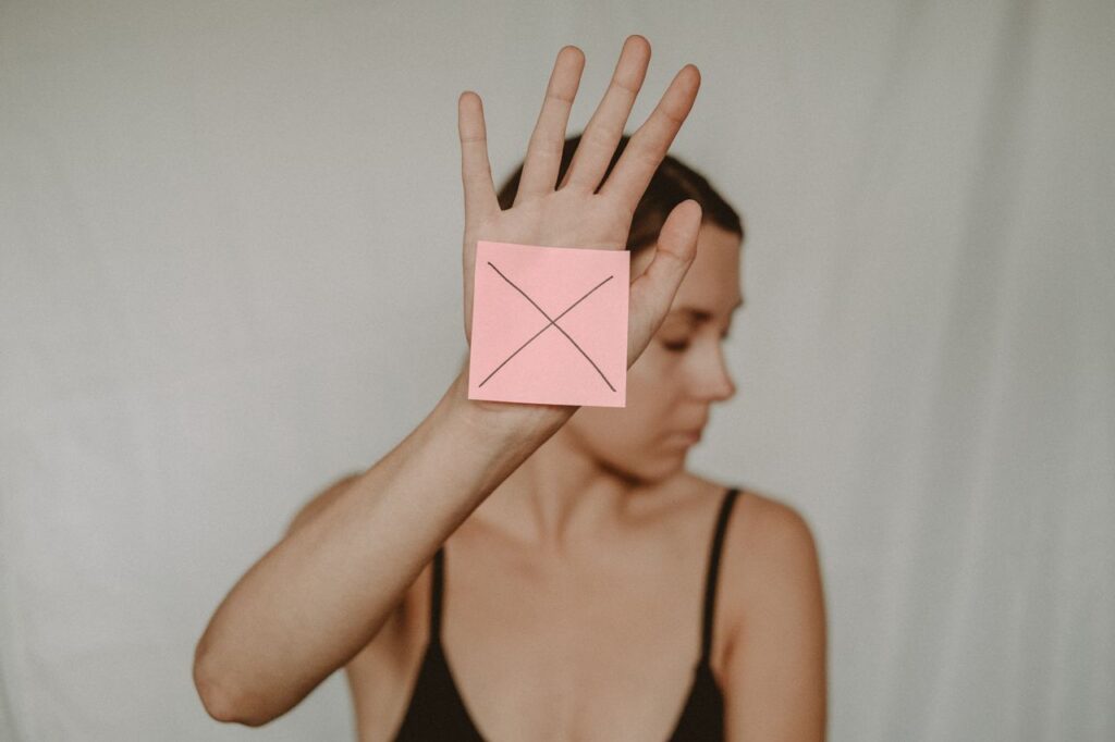 Young slender woman with closed eyes demonstrating sign stop with sticker on palm
